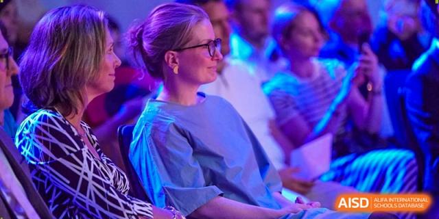 A teacher or parent sits in the audience and watches a student performance with a look of pride. Deutsche Botschaftsschule Peking