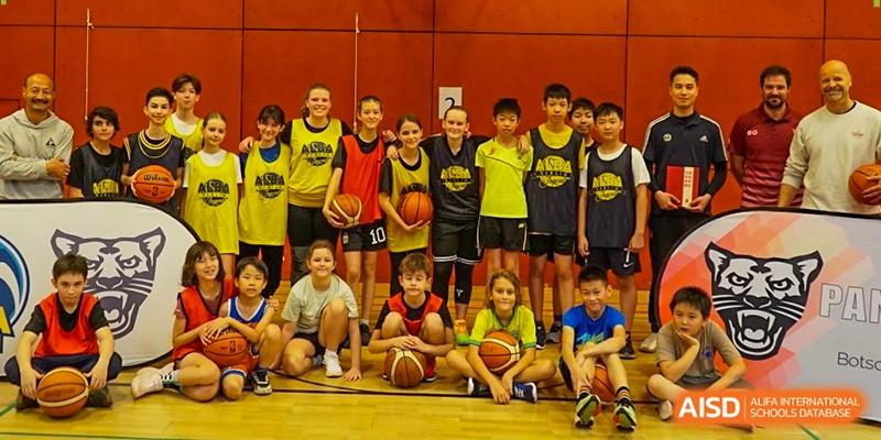 A diverse group of young students in basketball jerseys posing together on an indoor sports court at the Deutsche Botschaftsschule Peking.