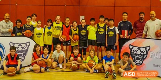 A diverse group of young students in basketball jerseys posing together on an indoor sports court at the Deutsche Botschaftsschule Peking.
