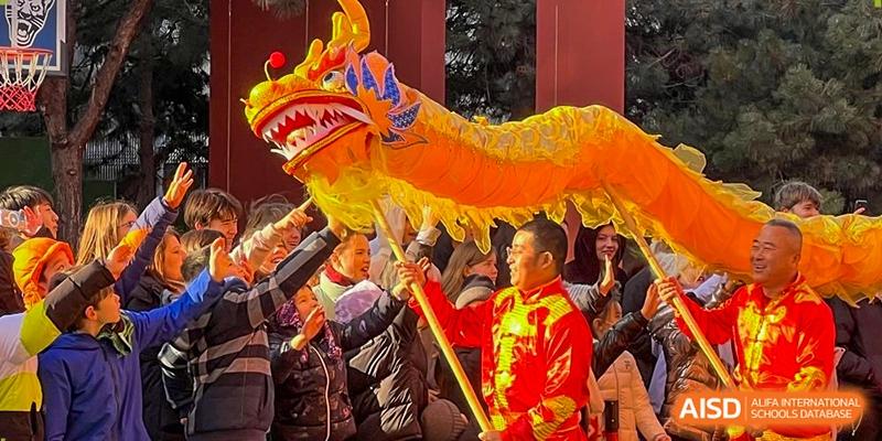 Students and a performer celebrate with a vibrant yellow dragon during a traditional cultural event at the Deutsche Botschaftsschule Peking.