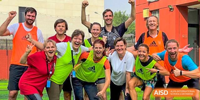 A group of smiling teachers and staff in athletic gear celebrate together outdoors at the Deutsche Botschaftsschule Peking.