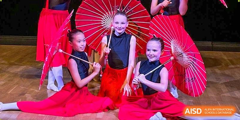 Three young girls in black and red dance costumes pose with traditional red parasols at the Deutsche Botschaftsschule Peking.
