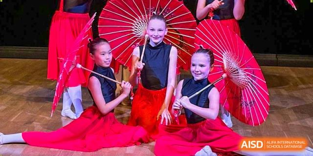 Three young girls in black and red dance costumes pose with traditional red parasols at the Deutsche Botschaftsschule Peking.