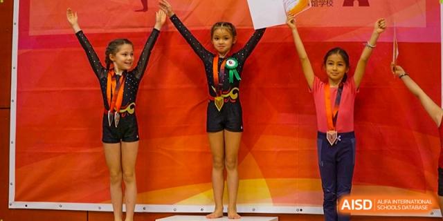 Three young gymnasts proudly display their medals and certificates after a performance at the Deutsche Botschaftsschule Peking.