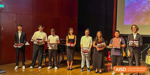 Five students stand on a stage holding awards during a formal school ceremony or graduation event. Deutsche Botschaftsschule Peking