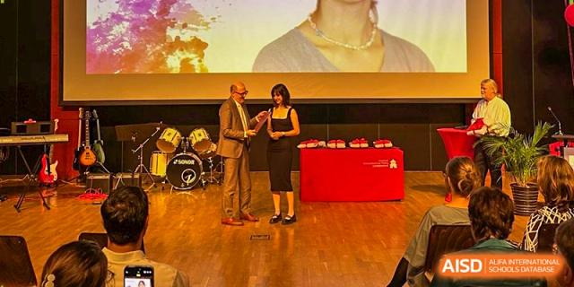 A student receives a diploma from a faculty member on stage during the 2025 graduation ceremony. Deutsche Botschaftsschule Peking