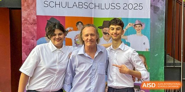 Two graduates pose for a joyful photo with a teacher in front of a "Schulabschluss 2025" banner. Deutsche Botschaftsschule Peking