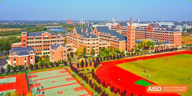 Aerial view of a sprawling modern campus with red brick buildings and a professional red running track at Harbin Meijia Foreign Language School.