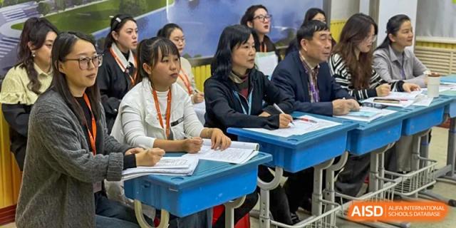 Three staff members sit at school desks and review academic materials during a professional development meeting at Harbin Meijia Foreign Language School.