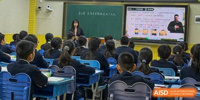 A teacher leads a lecture for a classroom full of attentive students seated at individual blue desks at Harbin Meijia Foreign Language School.