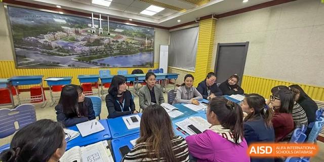 A group of educators sits at a blue table in a classroom, focused on a discussion during a collaborative meeting at Harbin Meijia Foreign Language School.