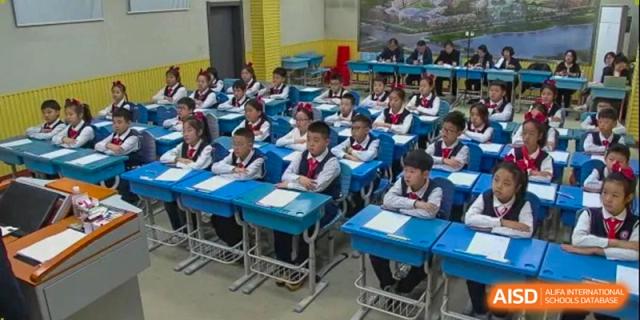 Students in navy uniforms sit attentively at individual blue desks in a bright, modern classroom at Harbin Meijia Foreign Language School.
