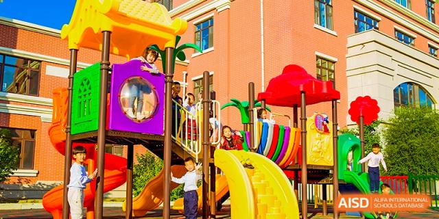 Young children play on a bright, colorful outdoor playground structure with slides on a sunny day at Harbin Meijia Foreign Language School.