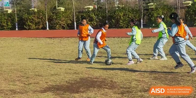 Two students in orange jerseys practice soccer drills on a grass field, focusing on ball control during an outdoor physical education class at Harbin Meijia Foreign Language School.