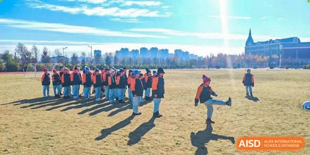 A line of students in matching winter athletic gear stands on a wide field under a clear blue sky during a morning exercise session at Harbin Meijia Foreign Language School.