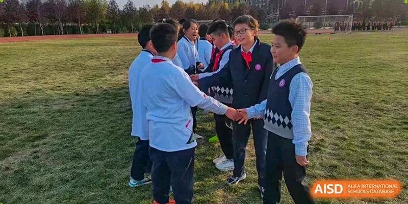 Students in school uniforms stand in a circle on the grass, reaching out to join hands during a team-building exercise at Harbin Meijia Foreign Language School.