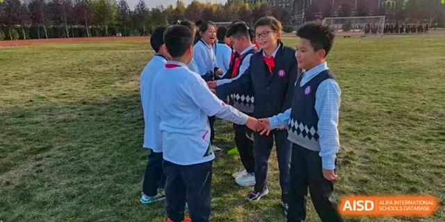 Students in school uniforms stand in a circle on the grass, reaching out to join hands during a team-building exercise at Harbin Meijia Foreign Language School.