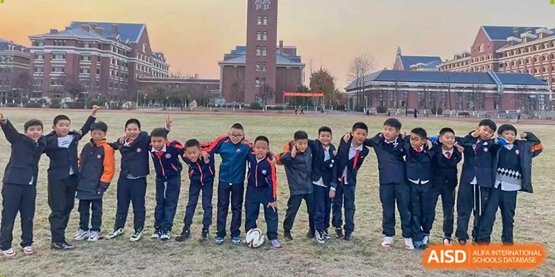 A group of boys in athletic jackets stands together on a sports field with a soccer ball, posing for a photo at Harbin Meijia Foreign Language School.