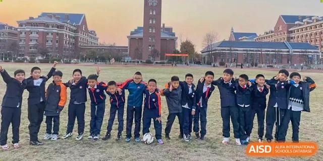 A group of boys in athletic jackets stands together on a sports field with a soccer ball, posing for a photo at Harbin Meijia Foreign Language School.