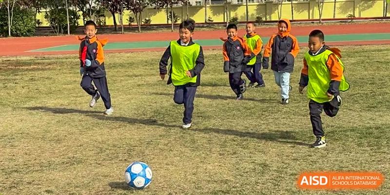 A student in a bright yellow jersey runs toward a soccer ball on a sunny day during an outdoor sports session at Harbin Meijia Foreign Language School.