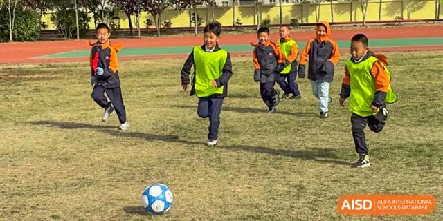 A student in a bright yellow jersey runs toward a soccer ball on a sunny day during an outdoor sports session at Harbin Meijia Foreign Language School.