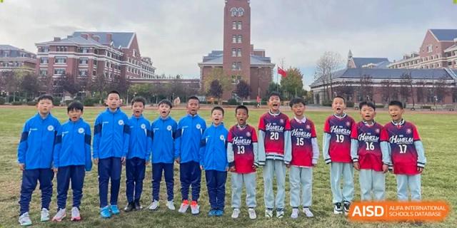 Students stand in a line on the sports field wearing various athletic jerseys with the brick school tower in the background at Harbin Meijia Foreign Language School.