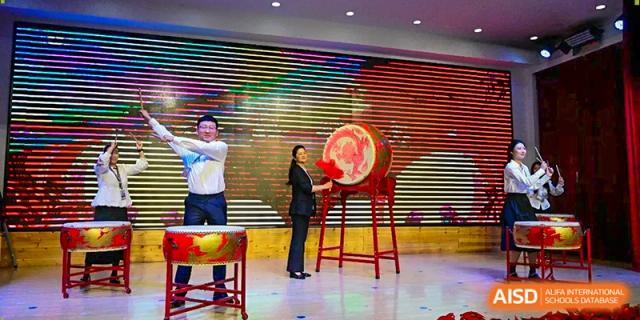 A performer stands next to a large traditional red drum on a stage during a cultural celebration event at Harbin Meijia Foreign Language School.