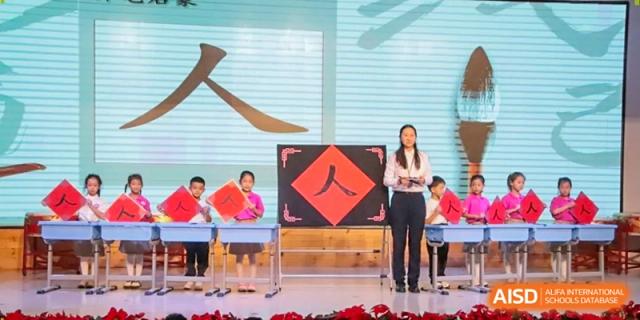 Students stand on a stage next to a large display featuring Chinese calligraphy characters during a language arts presentation at Harbin Meijia Foreign Language School.