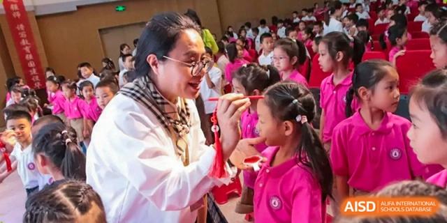 A teacher wearing glasses gently interacts with a young student in a pink shirt during a classroom activity at Harbin Meijia Foreign Language School.