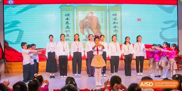 A young student performs a traditional salute on stage in front of a backdrop featuring historical artwork at Harbin Meijia Foreign Language School.