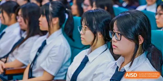 A side profile of a female student wearing glasses and a school uniform sitting in an auditorium at Maple Leaf International Schools - Hainan