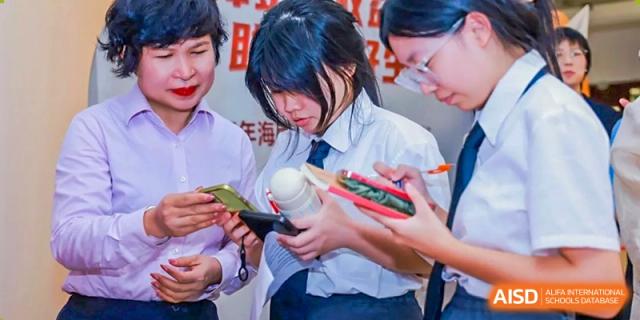 A female student in a white uniform shirt looking down at objects in her hands among a group of peers at Maple Leaf International Schools - Hainan