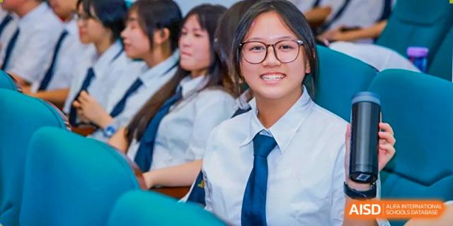 A close-up of a smiling female student with glasses sitting among classmates in a blue-seated auditorium at Maple Leaf International Schools - Hainan