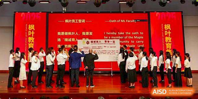 A group of people on a stage participating in a formal oath ceremony with a large banner in the background at Maple Leaf International Schools - Hainan