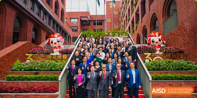 A large group of faculty and staff in professional attire posing for a group photo on outdoor stairs at Maple Leaf International Schools - Hainan