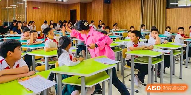 A teacher in a pink jacket interacting with students at green desks in a classroom setting at Maple Leaf International Schools - Hainan