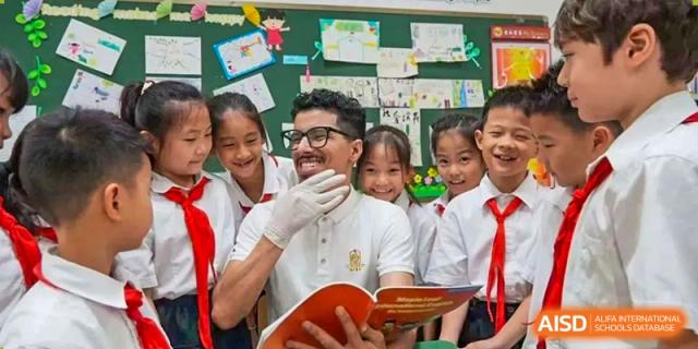 A male teacher wearing white gloves smiling while reading a book to three young students at Maple Leaf International Schools - Hainan