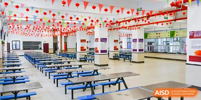 A large and empty school cafeteria with blue tables and red decorations hanging from the ceiling at Maple Leaf International Schools - Hainan