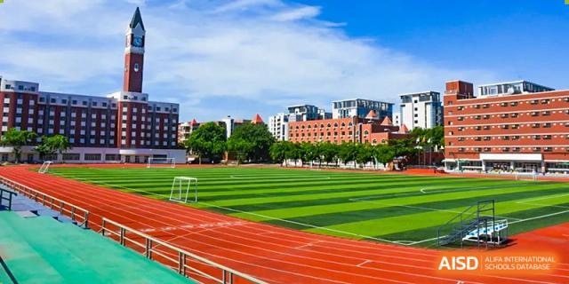 An expansive view of a green sports field and red running track under a bright blue sky at Maple Leaf International Schools - Hainan