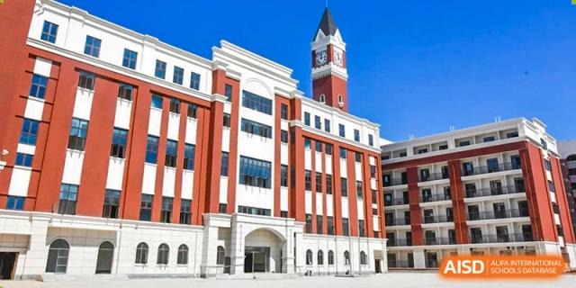 A modern school building with red and white architecture featuring a prominent clock tower at Maple Leaf International Schools - Hainan