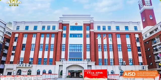 Front view of a grand multi-story school building with red and white columns and a central entrance at Maple Leaf International Schools - Hainan