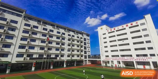 Wide shot of a modern white school building overlooking a green athletic field and running track at Maple Leaf International Schools - Hainan
