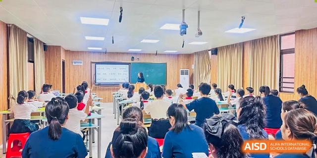 Students sitting at desks in a large lecture hall while a teacher presents at the front of the room at Maple Leaf International Schools - Hainan