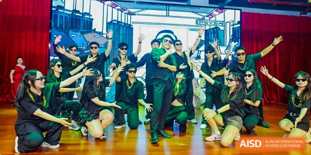 A group of students in dark green performance outfits and sunglasses posing together on a wooden stage at Maple Leaf International Schools - Hainan