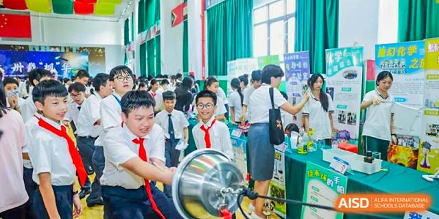 Students gathered around a science demonstration involving a silver metal hemisphere in a bright room at Maple Leaf International Schools - Hainan