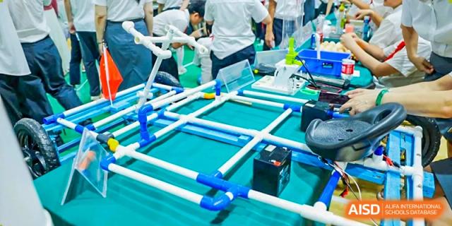 Close-up of a blue and white PVC pipe structure and electronic components on a green table for a project at Maple Leaf International Schools - Hainan