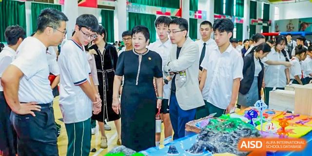 School officials and guests walking through an exhibition area and looking at student displays at Maple Leaf International Schools - Hainan