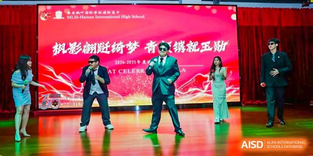 A male student in a sharp green suit and sunglasses performs on a brightly lit stage during a school gala Maple Leaf International Schools - Hainan