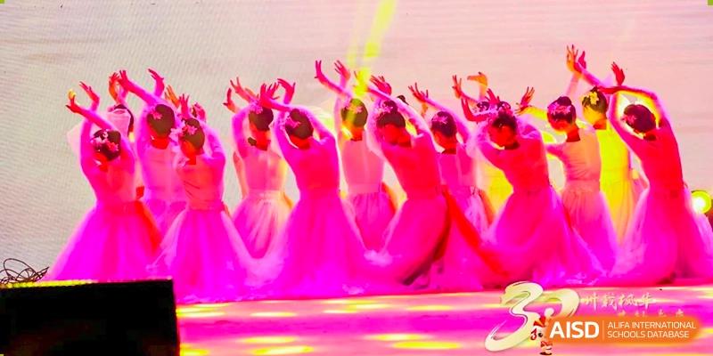 A group of dancers in vibrant pink costumes perform a synchronized routine on stage under bright lights Maple Leaf International Schools - Hainan