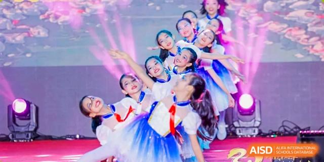 Young students in white and blue dresses with red scarves perform a group dance on stage Maple Leaf International Schools - Hainan